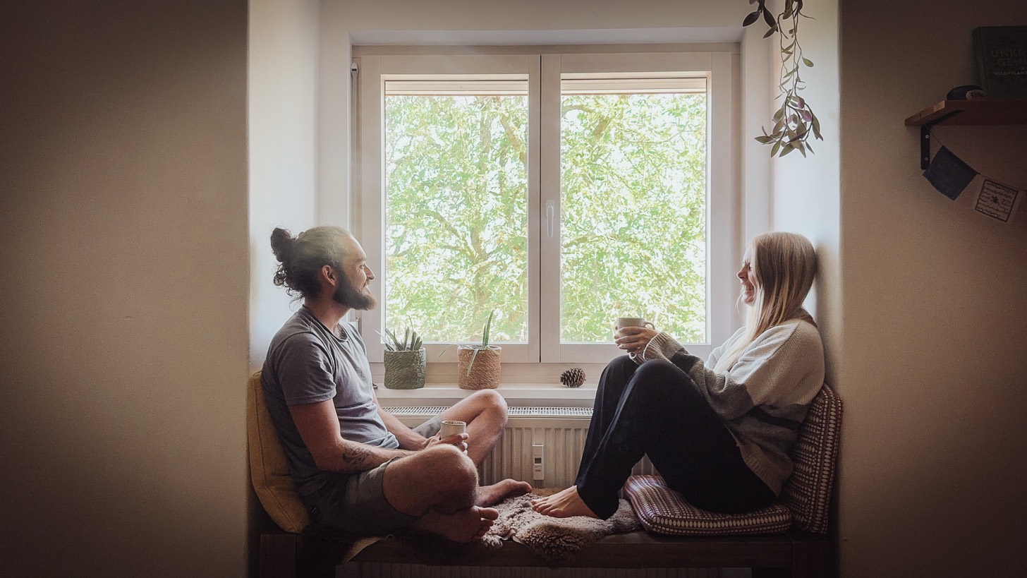 Michael Storz und Alexandra Kaschny sitzen mit Tassen in der Hand an einem Fenster im Gespräch